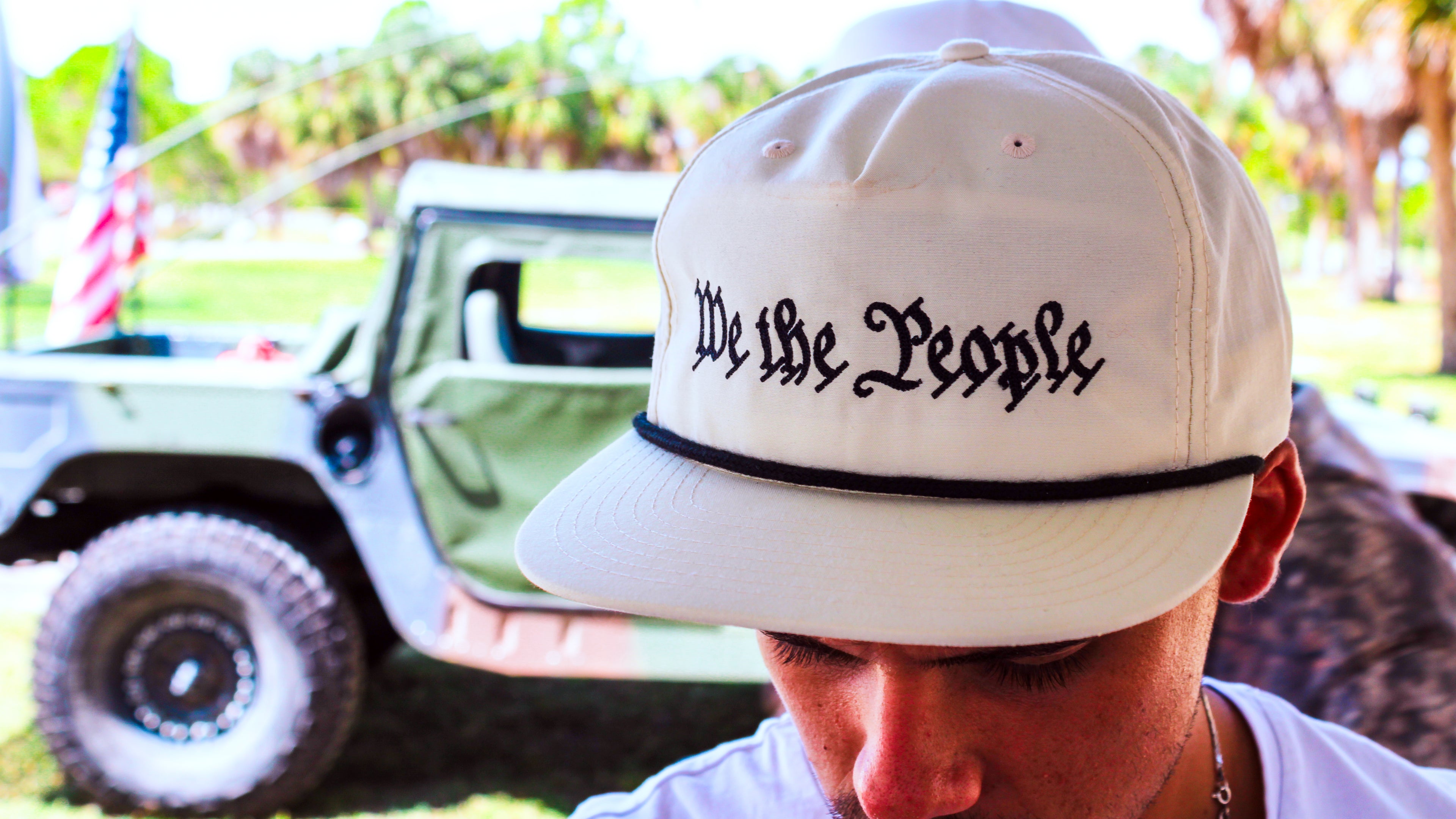 Person wearing a cap with 'We the People' text, standing in front of a vintage truck.
