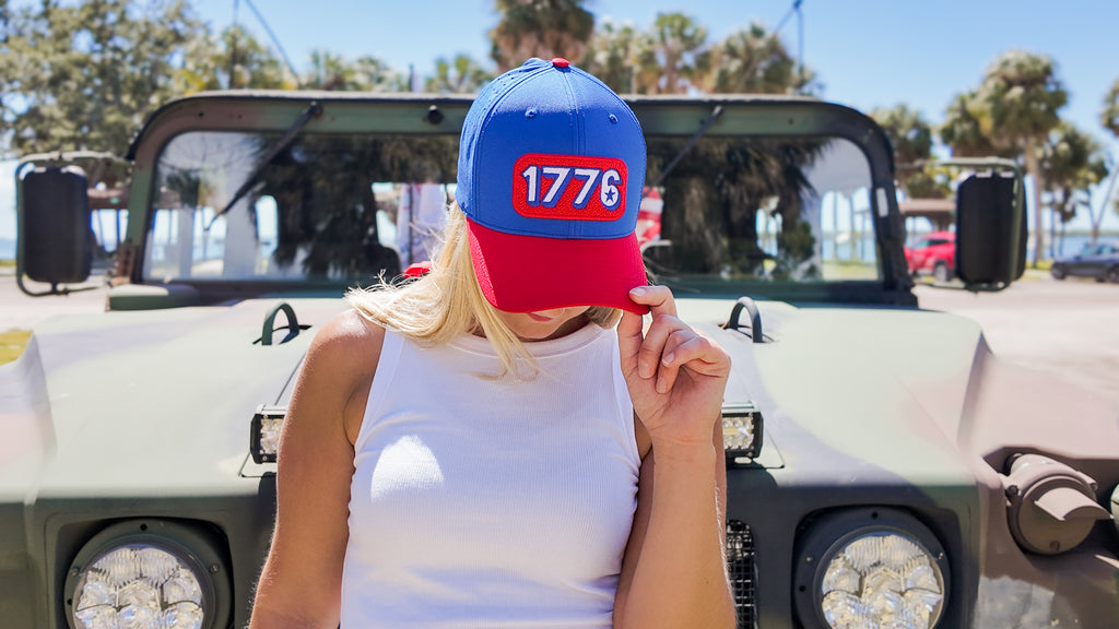 Person wearing a blue and red cap with '1776' on it, standing in front of a vehicle.