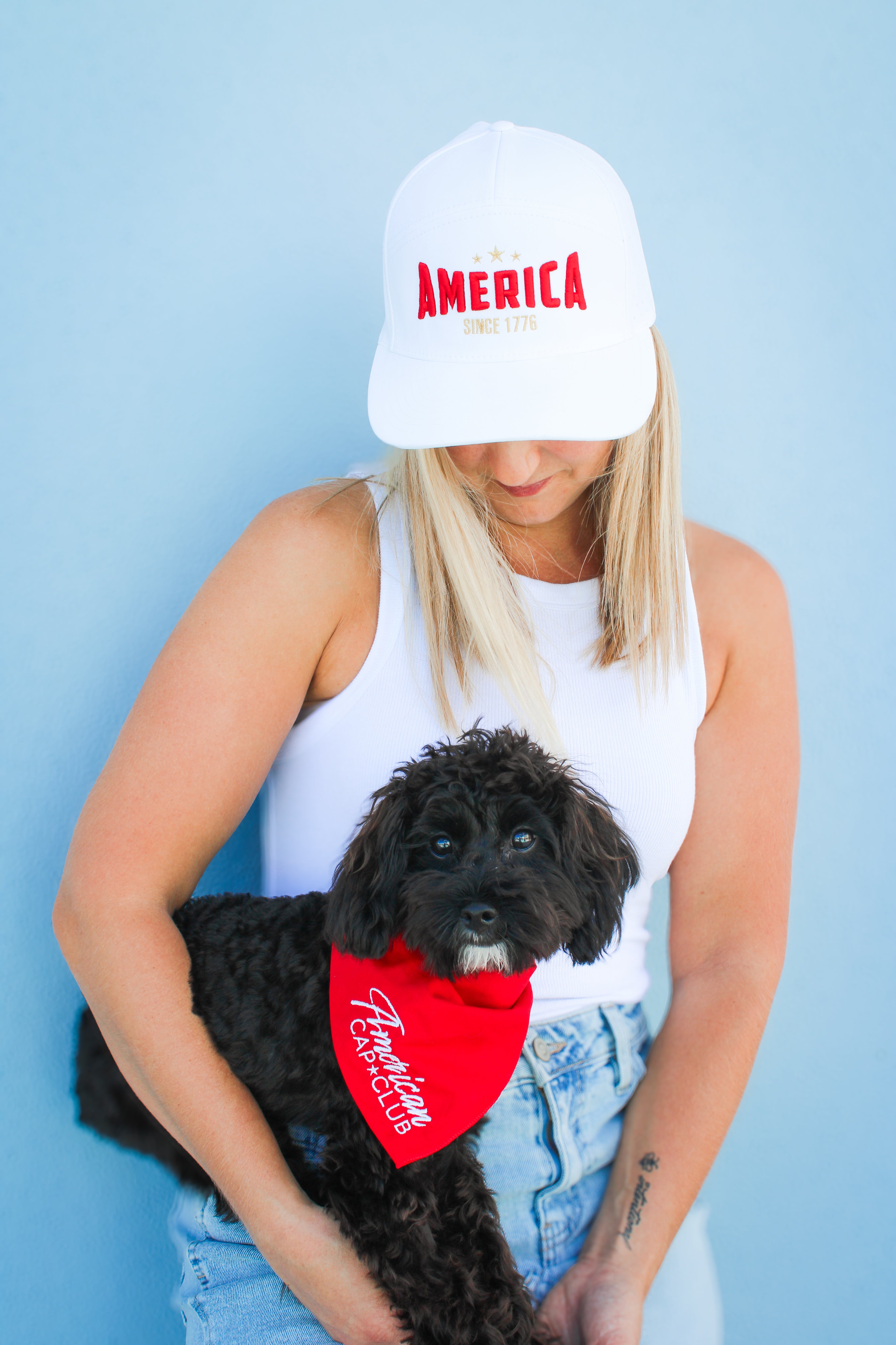 Person holding a black dog wearing a red bandana with 'AMERICA' text on a blue background