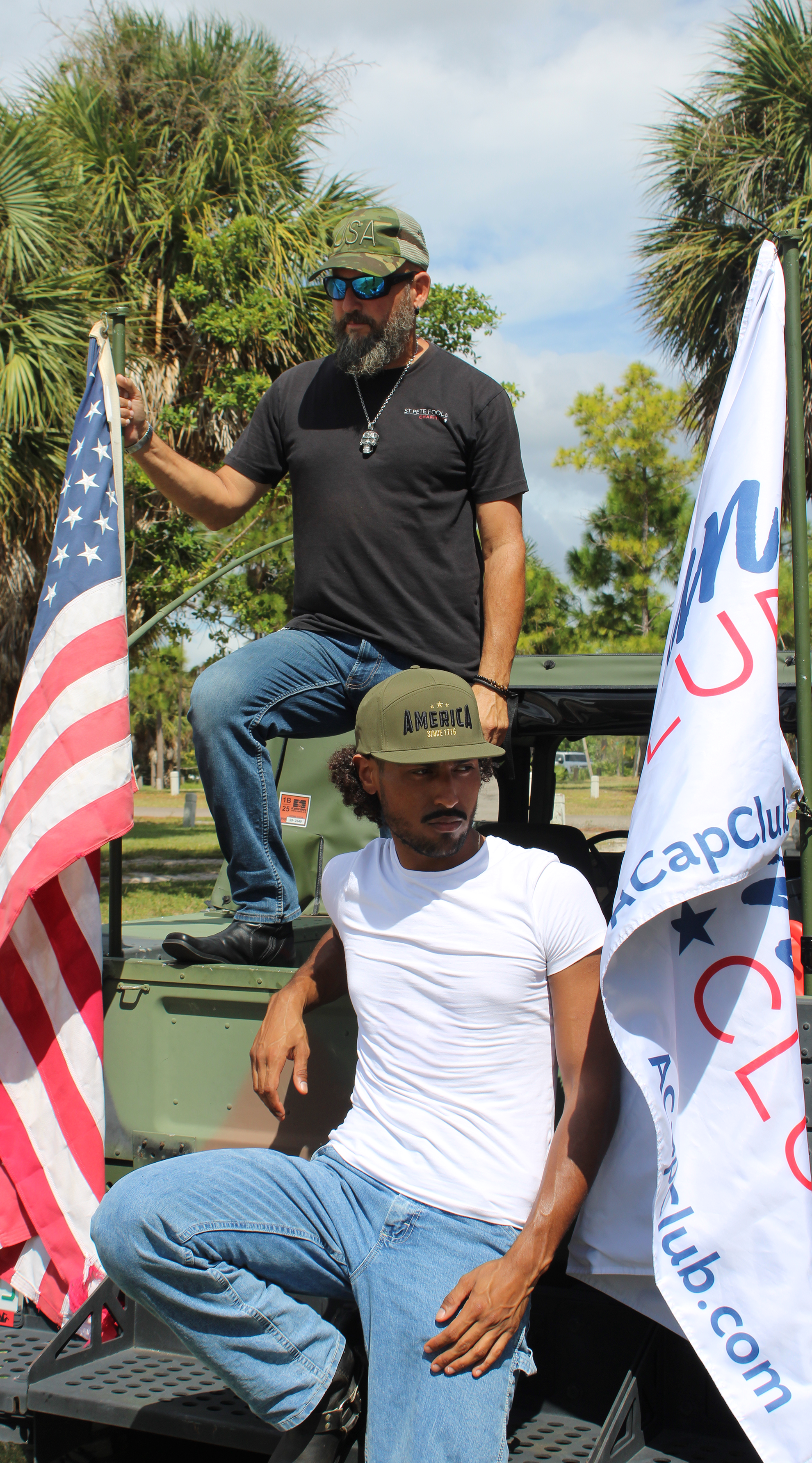 Two men on an army vehicle with American flag and American hats