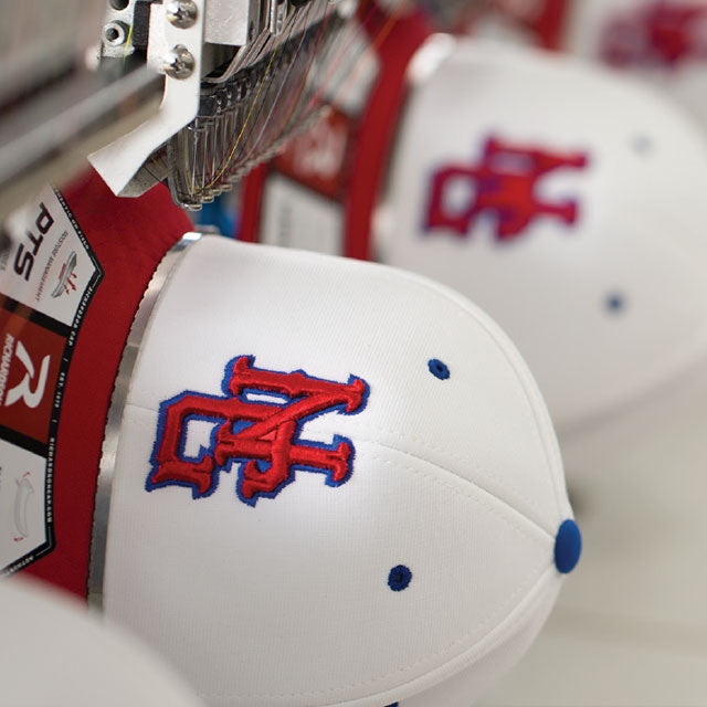 Embroidery machine stitching a logo onto a white cap with red and blue design by American Cap Club